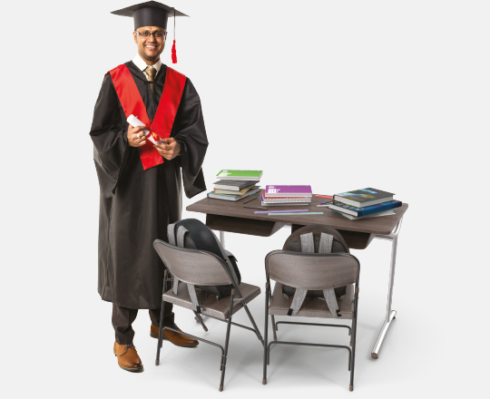 University graduate standing by desk with books on